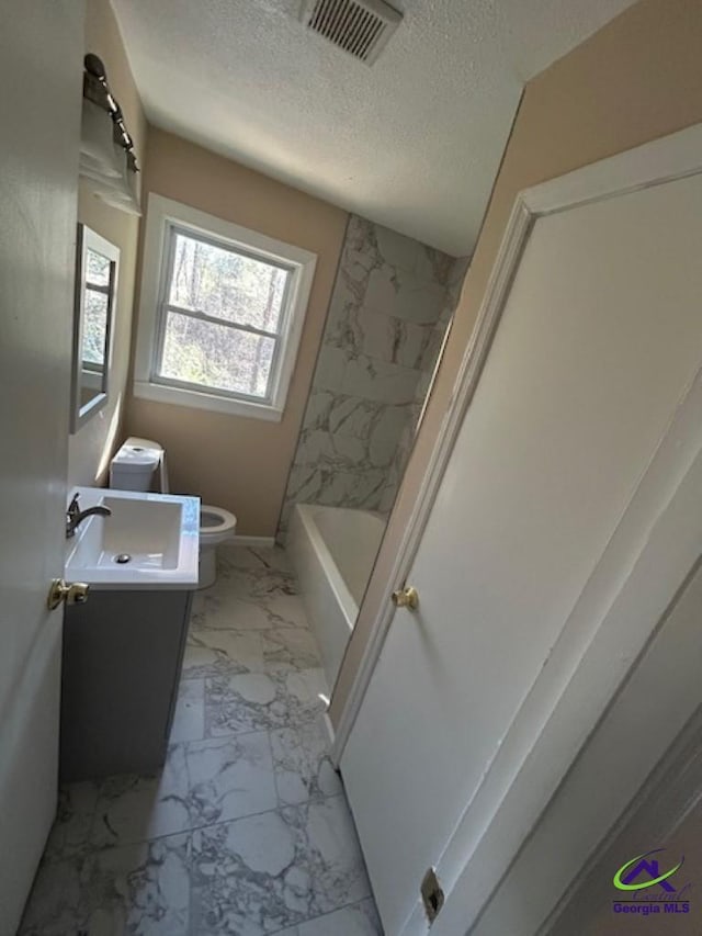 full bathroom with vanity, a textured ceiling, tiled shower / bath combo, and toilet