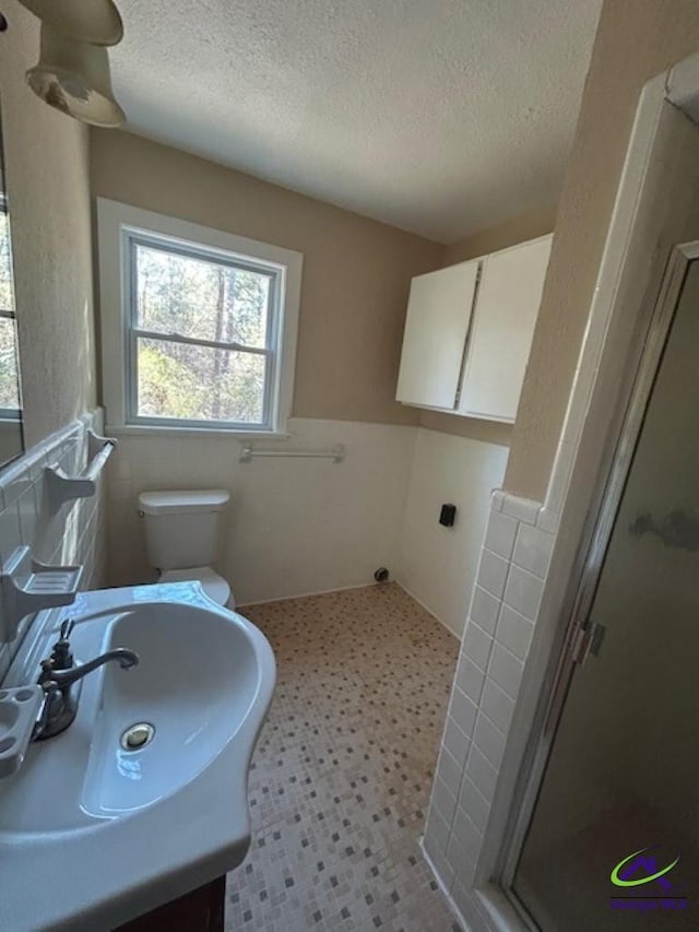 bathroom with tile walls, a shower with door, toilet, and a textured ceiling