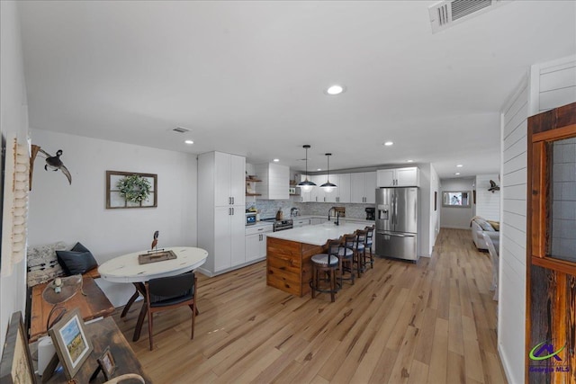 kitchen featuring appliances with stainless steel finishes, hanging light fixtures, light hardwood / wood-style floors, white cabinets, and a kitchen island