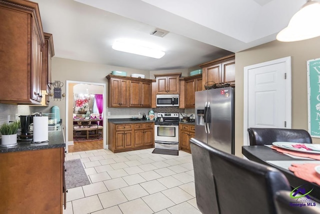 306 Lovorn Cir, Warner Robins, GA 31088 - kitchen featuring stainless steel appliances, tasteful backsplash, dark countertops, brown cabinets, and light tile patterned floors