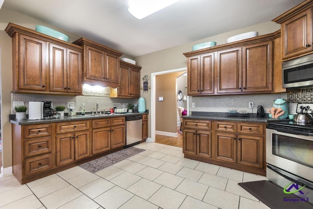 306 Lovorn Cir, Warner Robins, GA 31088 - kitchen with appliances with stainless steel finishes, decorative backsplash, baseboards, light tile patterned floors, and brown cabinetry