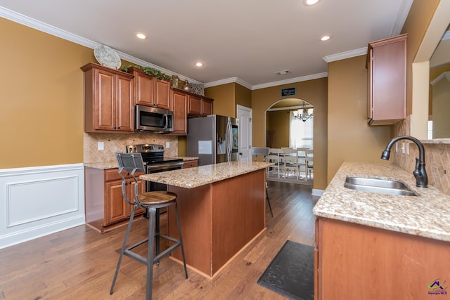 kitchen with sink, stainless steel appliances, a kitchen breakfast bar, ornamental molding, and a kitchen island