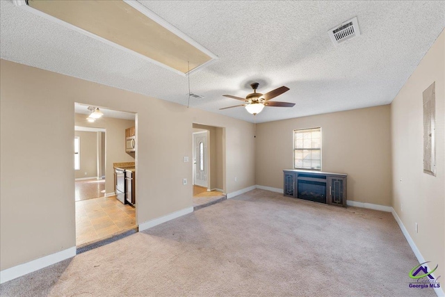 unfurnished living room featuring ceiling fan, a fireplace, light colored carpet, and a textured ceiling