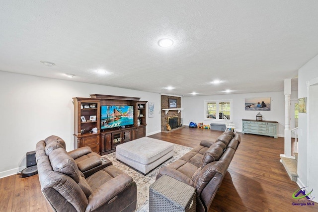 living room with hardwood / wood-style flooring, a textured ceiling, a fireplace, and ornate columns