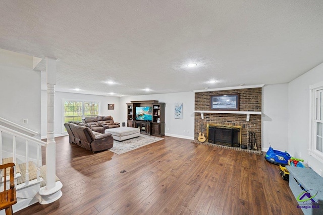 living room featuring wood-type flooring, a fireplace, decorative columns, and a textured ceiling