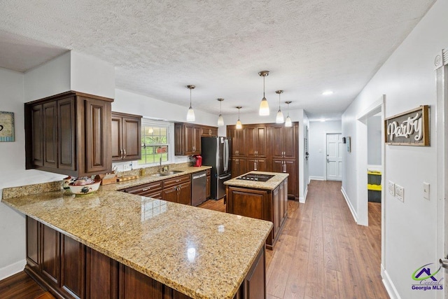 kitchen with appliances with stainless steel finishes, decorative light fixtures, hardwood / wood-style flooring, a center island, and kitchen peninsula