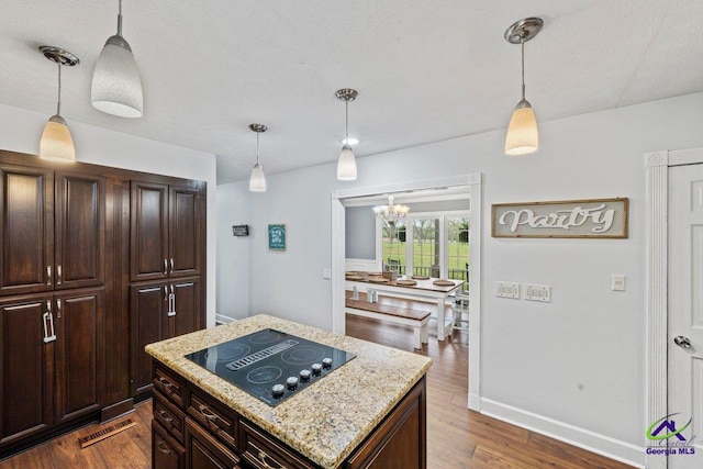 kitchen with dark hardwood / wood-style floors, pendant lighting, a center island, black electric stovetop, and light stone counters