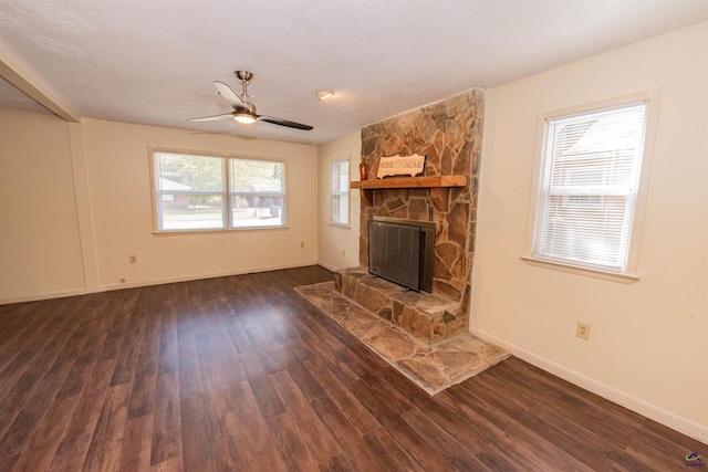 unfurnished living room with a stone fireplace, dark wood-type flooring, and ceiling fan