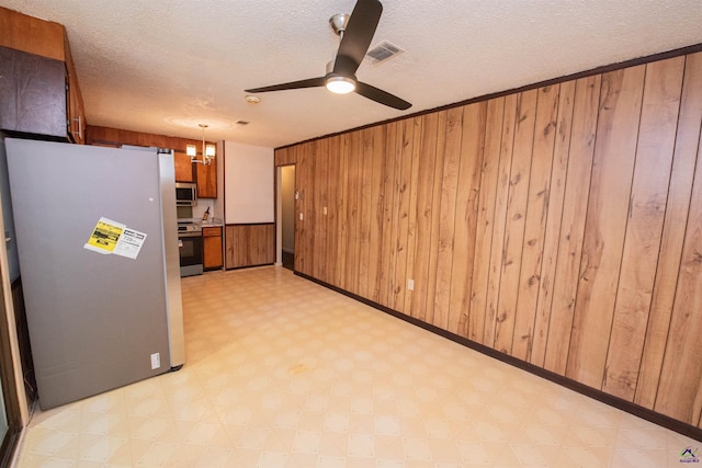 kitchen featuring wood walls, decorative light fixtures, a textured ceiling, appliances with stainless steel finishes, and ceiling fan with notable chandelier