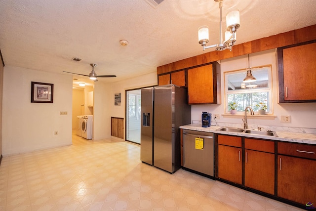 kitchen featuring sink, hanging light fixtures, washer and clothes dryer, stainless steel appliances, and a textured ceiling