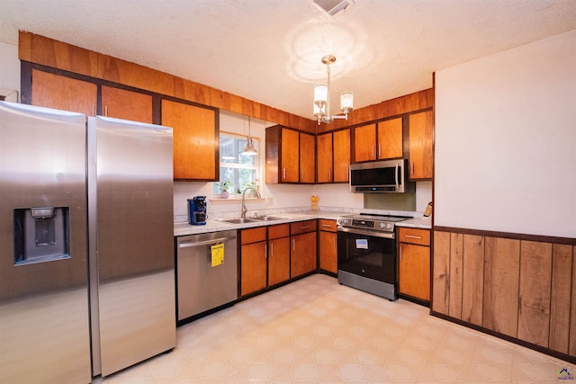 kitchen with pendant lighting, sink, appliances with stainless steel finishes, an inviting chandelier, and a textured ceiling