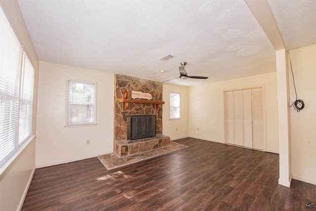 unfurnished living room featuring ceiling fan, a stone fireplace, a textured ceiling, and dark hardwood / wood-style flooring