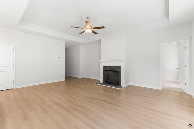 687 Jasmine Dr, Macon, GA 31211 - unfurnished living room featuring a tray ceiling, a ceiling fan, light wood-type flooring, a fireplace with raised hearth, and baseboards