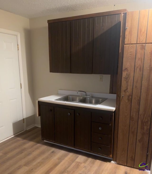 kitchen featuring dark brown cabinetry, sink, a textured ceiling, and light wood-type flooring