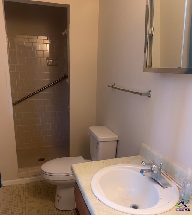 bathroom with a tile shower, vanity, tile patterned floors, and toilet