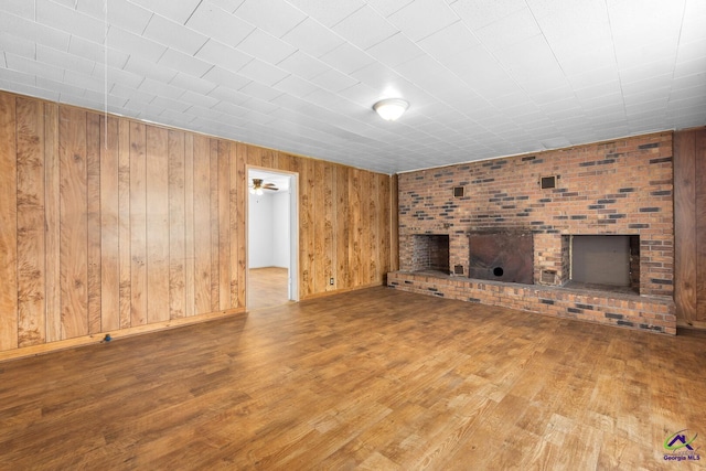 unfurnished living room featuring ceiling fan, wooden walls, a fireplace, and hardwood / wood-style floors