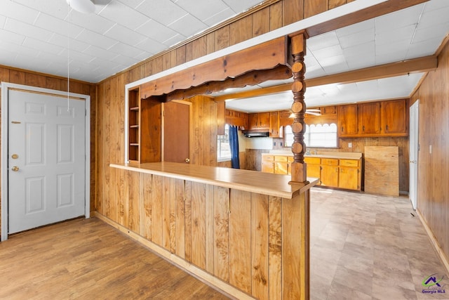 kitchen featuring ventilation hood, wood walls, beam ceiling, and kitchen peninsula