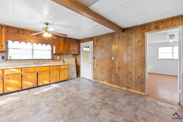 kitchen featuring beamed ceiling, sink, ceiling fan, and wood walls