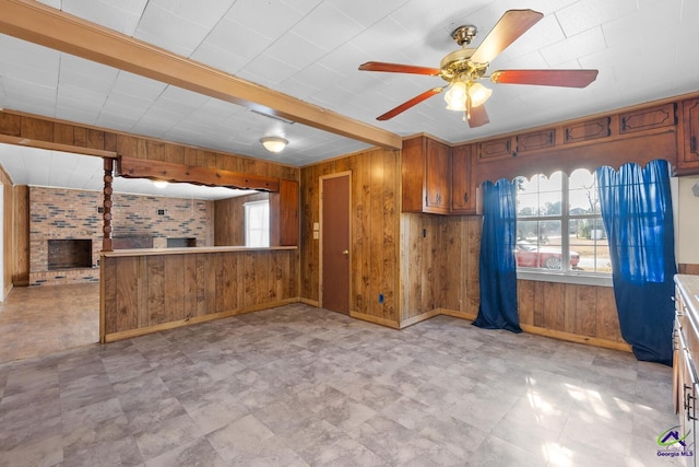 kitchen with wood walls, kitchen peninsula, beamed ceiling, ceiling fan, and a fireplace