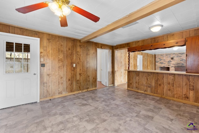 interior space featuring ceiling fan, beam ceiling, and wood walls