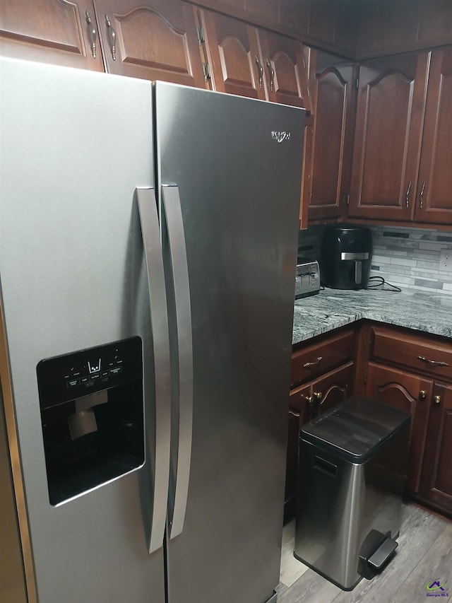 kitchen featuring stone countertops, stainless steel fridge, decorative backsplash, light hardwood / wood-style floors, and dark brown cabinetry