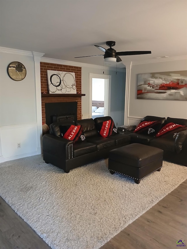 living room featuring a brick fireplace, crown molding, wood-type flooring, and ceiling fan