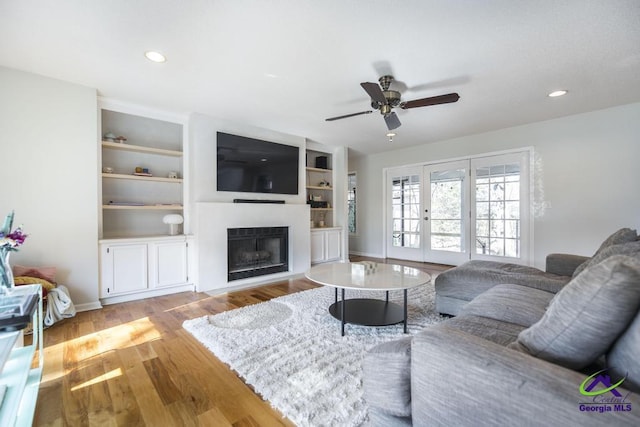 living room with french doors, built in shelves, ceiling fan, and light hardwood / wood-style flooring