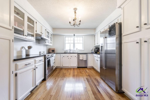 kitchen with light wood-type flooring, white cabinets, a notable chandelier, stainless steel appliances, and a textured ceiling