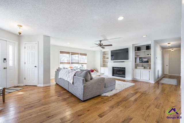 living room with ceiling fan, built in features, light hardwood / wood-style floors, and a textured ceiling