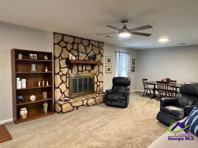 living room featuring light carpet, a stone fireplace, and ceiling fan