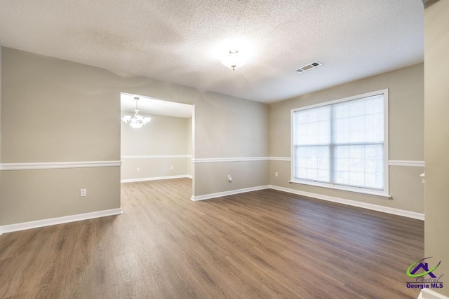 spare room featuring wood-type flooring, a textured ceiling, and a chandelier