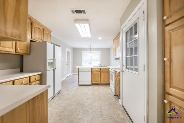 kitchen with sink, a skylight, kitchen peninsula, pendant lighting, and white appliances