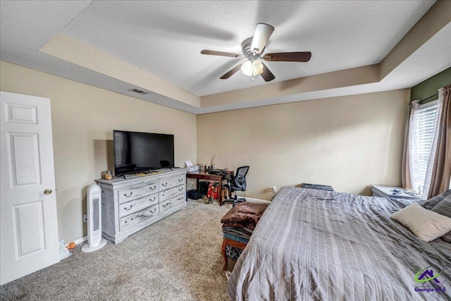 carpeted bedroom with ceiling fan, a tray ceiling, and a textured ceiling