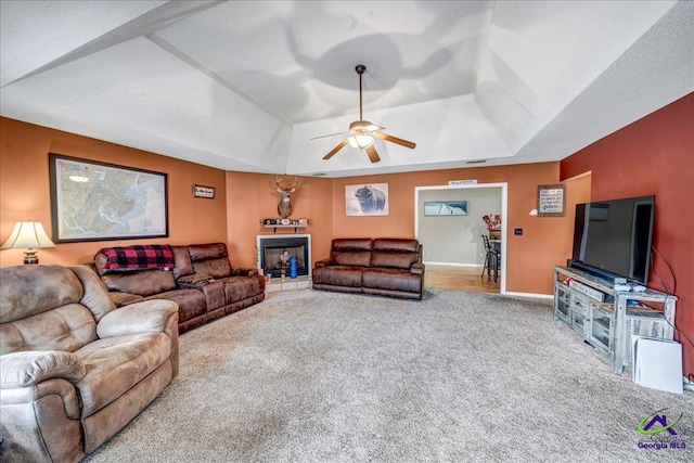 carpeted living room featuring a raised ceiling and ceiling fan