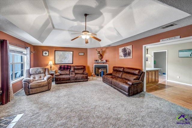 carpeted living room with a raised ceiling, ceiling fan, and a textured ceiling