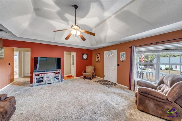 living room with a raised ceiling, ceiling fan, carpet flooring, and a textured ceiling