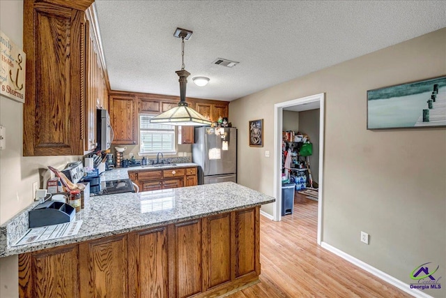 kitchen with sink, kitchen peninsula, pendant lighting, stainless steel appliances, and light stone countertops