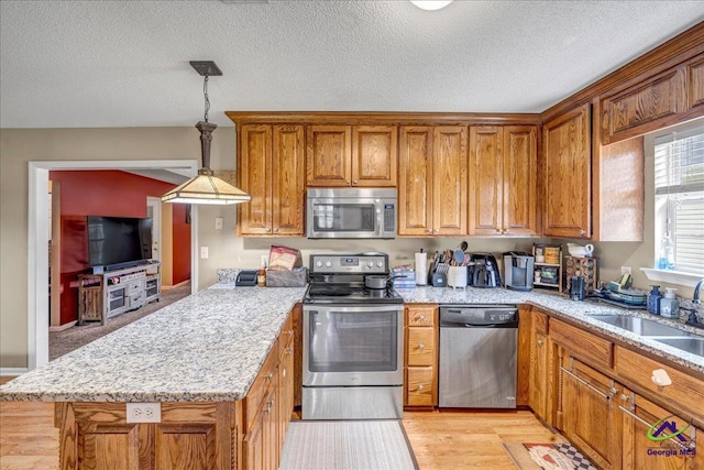 kitchen with sink, appliances with stainless steel finishes, hanging light fixtures, light hardwood / wood-style floors, and a textured ceiling