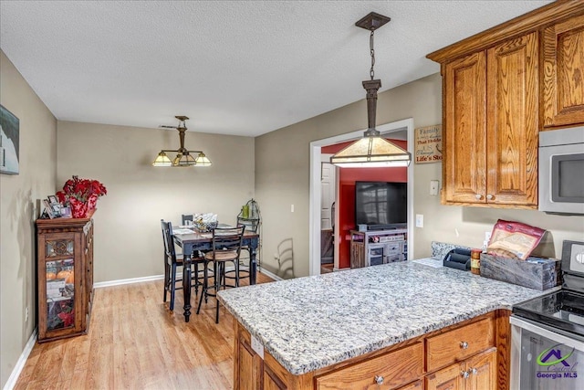 kitchen with stainless steel appliances, light hardwood / wood-style floors, hanging light fixtures, and a textured ceiling