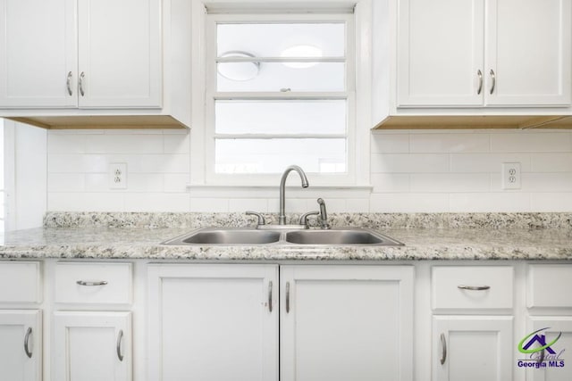 kitchen with tasteful backsplash, light stone countertops, sink, and white cabinets