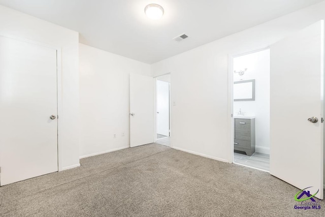 unfurnished bedroom featuring ensuite bath and light colored carpet