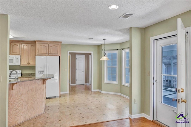 kitchen with light brown cabinetry, decorative light fixtures, kitchen peninsula, white appliances, and light stone countertops