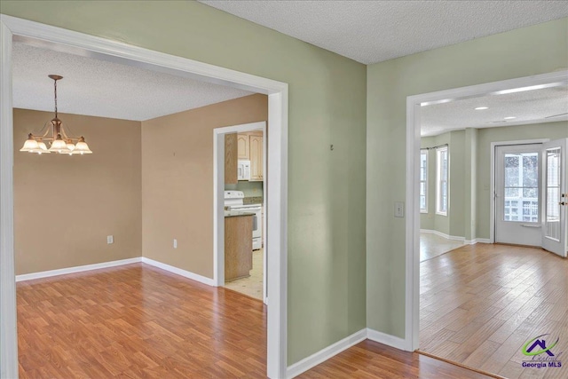 empty room with an inviting chandelier, light hardwood / wood-style floors, and a textured ceiling