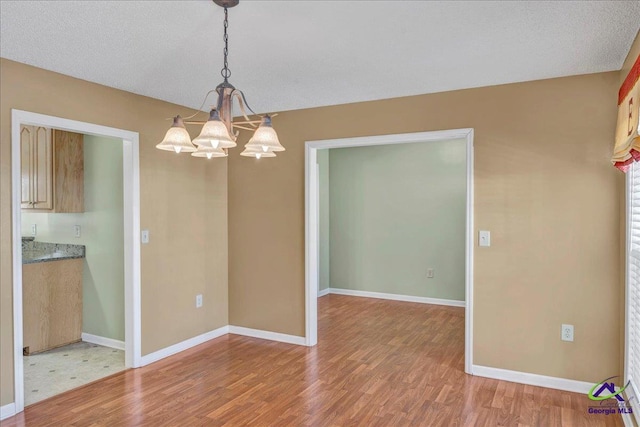 unfurnished dining area featuring a textured ceiling, wood-type flooring, and a chandelier