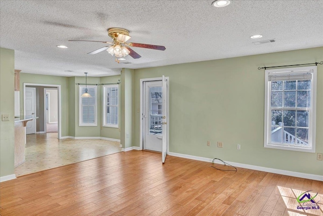 empty room with ceiling fan, a wealth of natural light, a textured ceiling, and light wood-type flooring