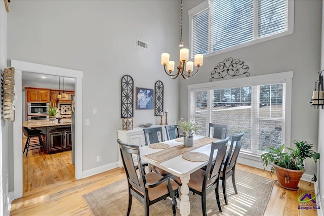 dining room with a high ceiling, an inviting chandelier, and light wood-type flooring