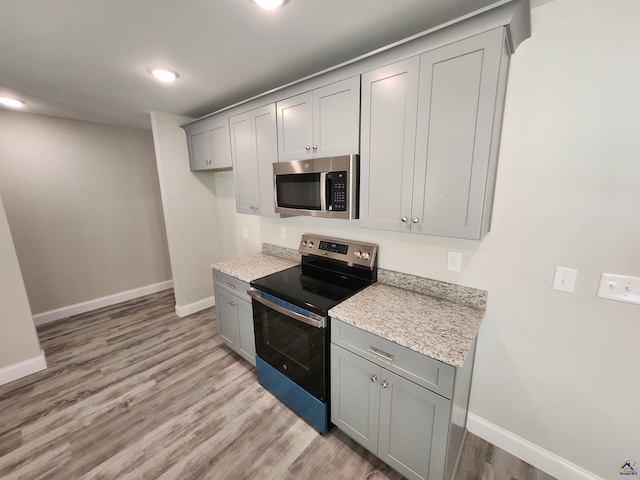 kitchen featuring baseboards, appliances with stainless steel finishes, gray cabinets, light stone countertops, and light wood finished floors