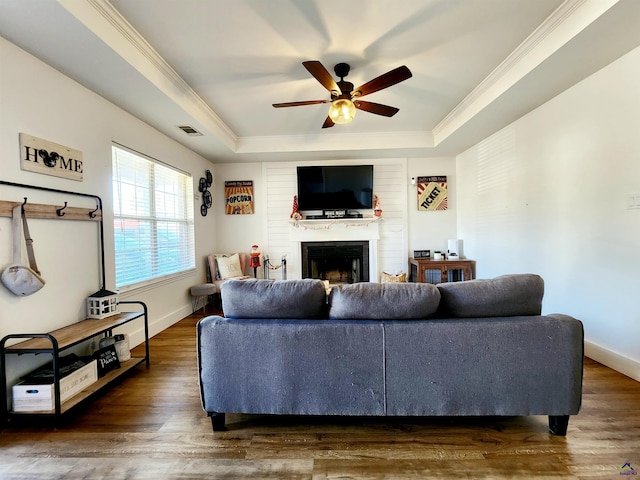 living room featuring ceiling fan, dark hardwood / wood-style floors, a tray ceiling, a fireplace, and ornamental molding