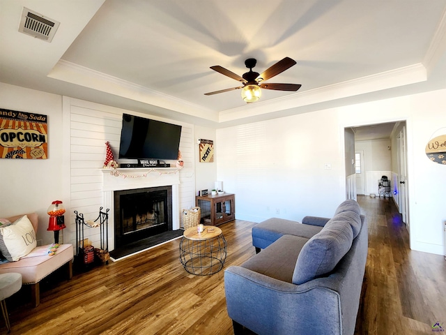 living room with crown molding, a large fireplace, hardwood / wood-style floors, and a tray ceiling