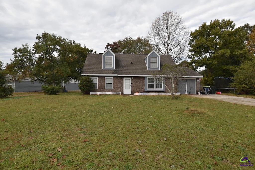 cape cod-style house featuring a garage, a trampoline, and a front lawn